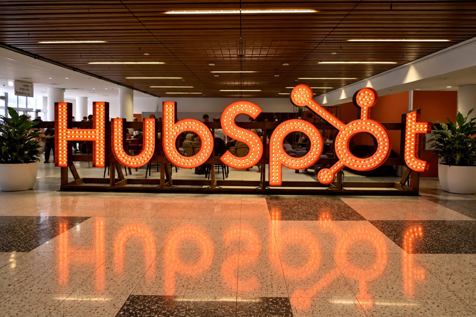 The HubSpot sign in bulb-lit letters across an office atrium, reflected in the floor.