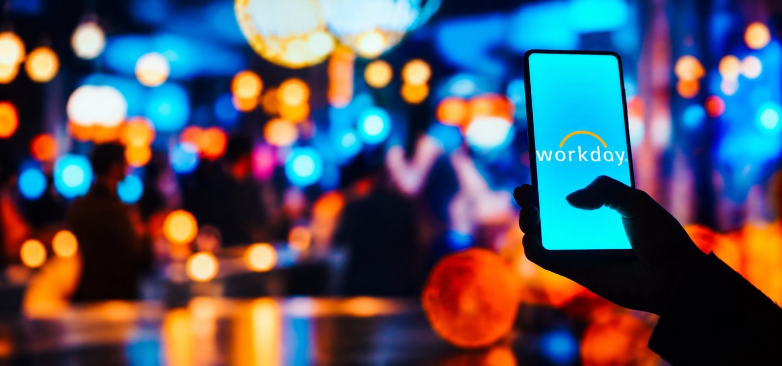 A phone held up in a crowd at night, the Workday mark on its screen against bokeh.